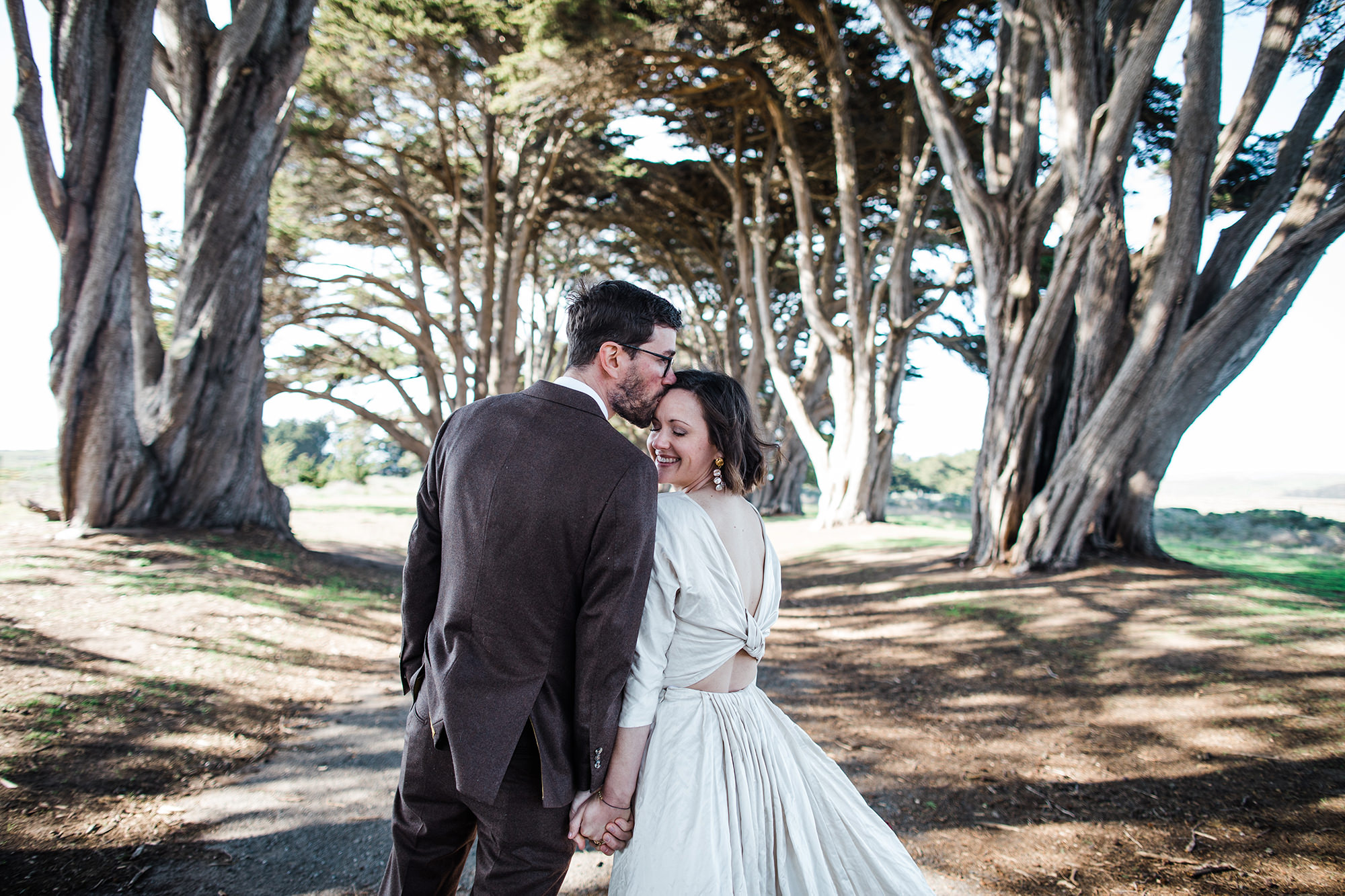 Groom sweetly kisses bride on forehead in the Cypress Tree Tunnel for Point Reyes Elopement.