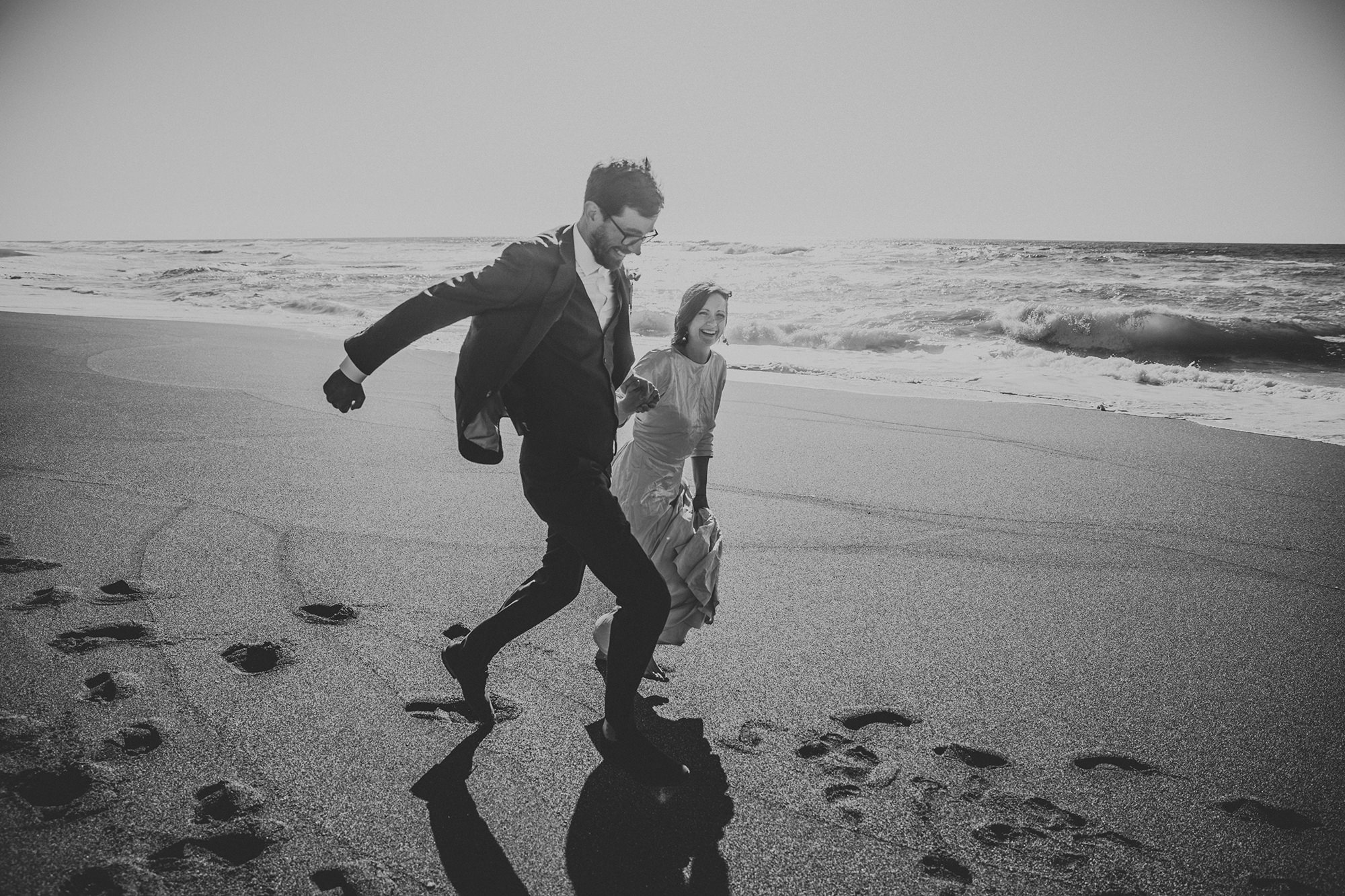 BW photo of bride and groom running on beach for California elopement