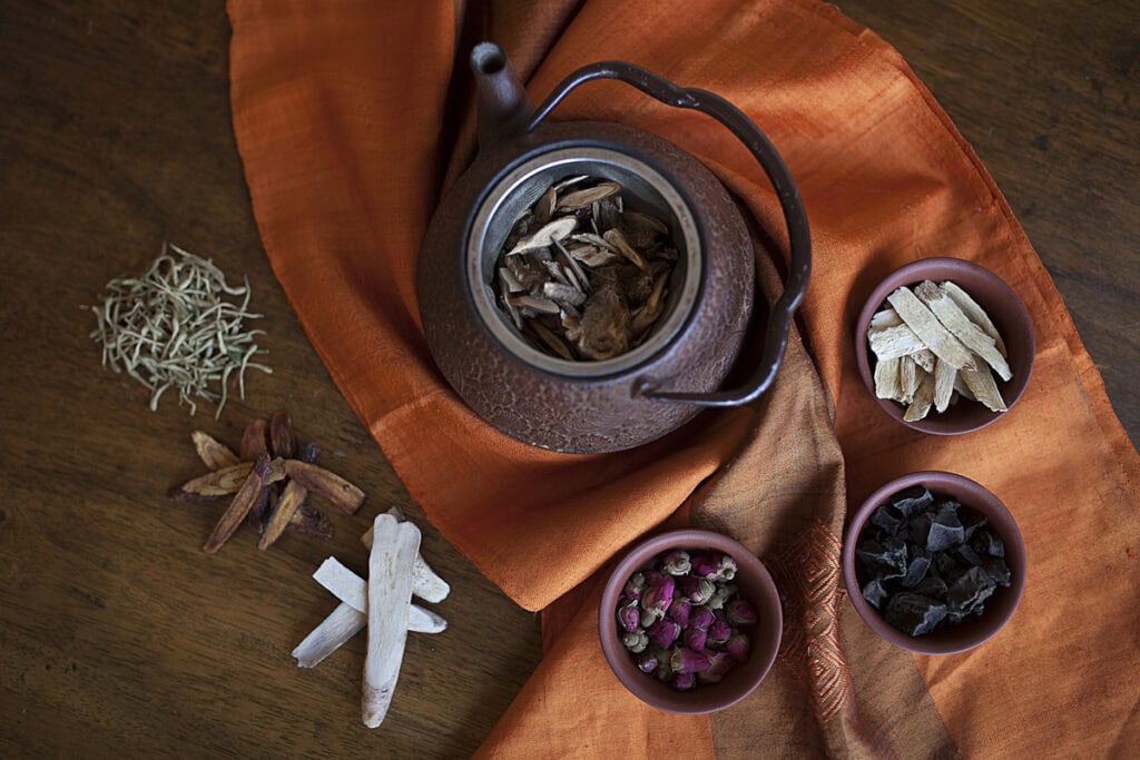 Herbal tea in a teapot with assorted dried herbs and flowers, promoting health and wellness.