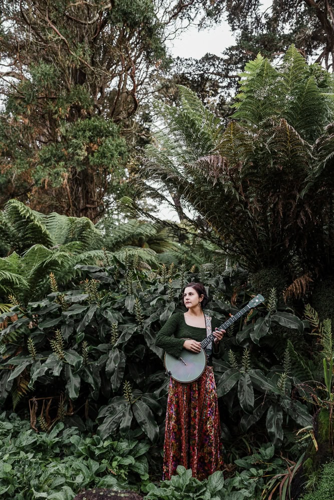 Woman playing guitar in lush green forest for branding photoshoot.