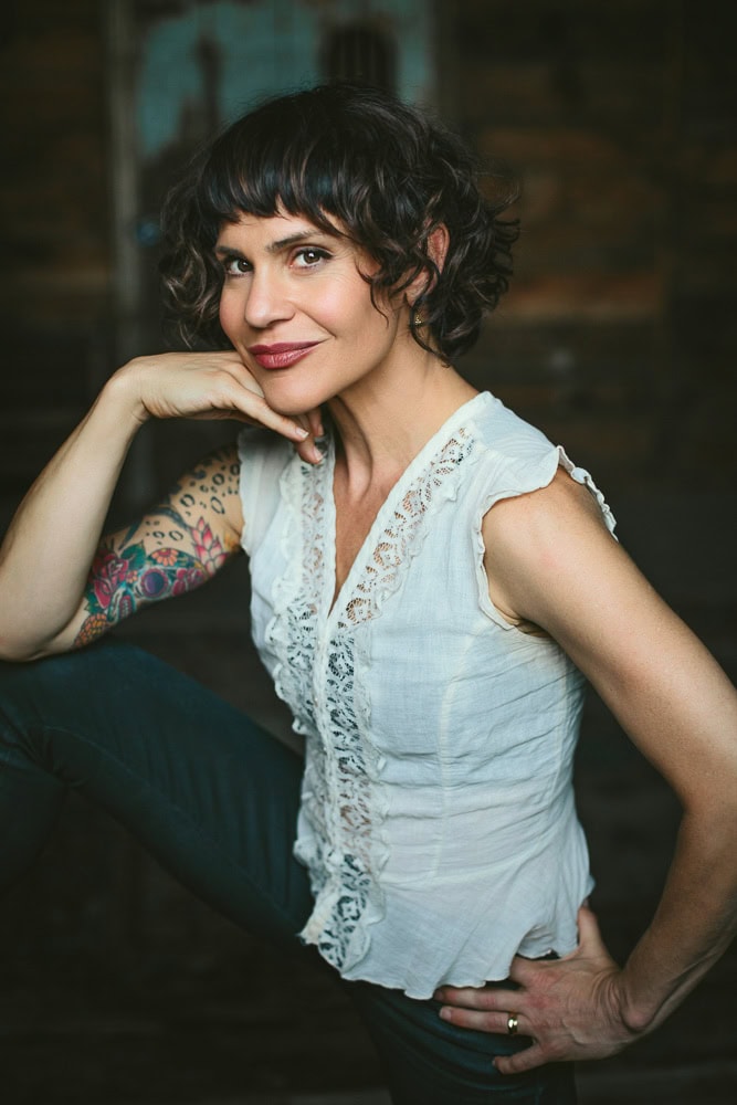 Woman with dark curly hair and colorful tattoo, posing confidently indoors for her yoga studio branding photography