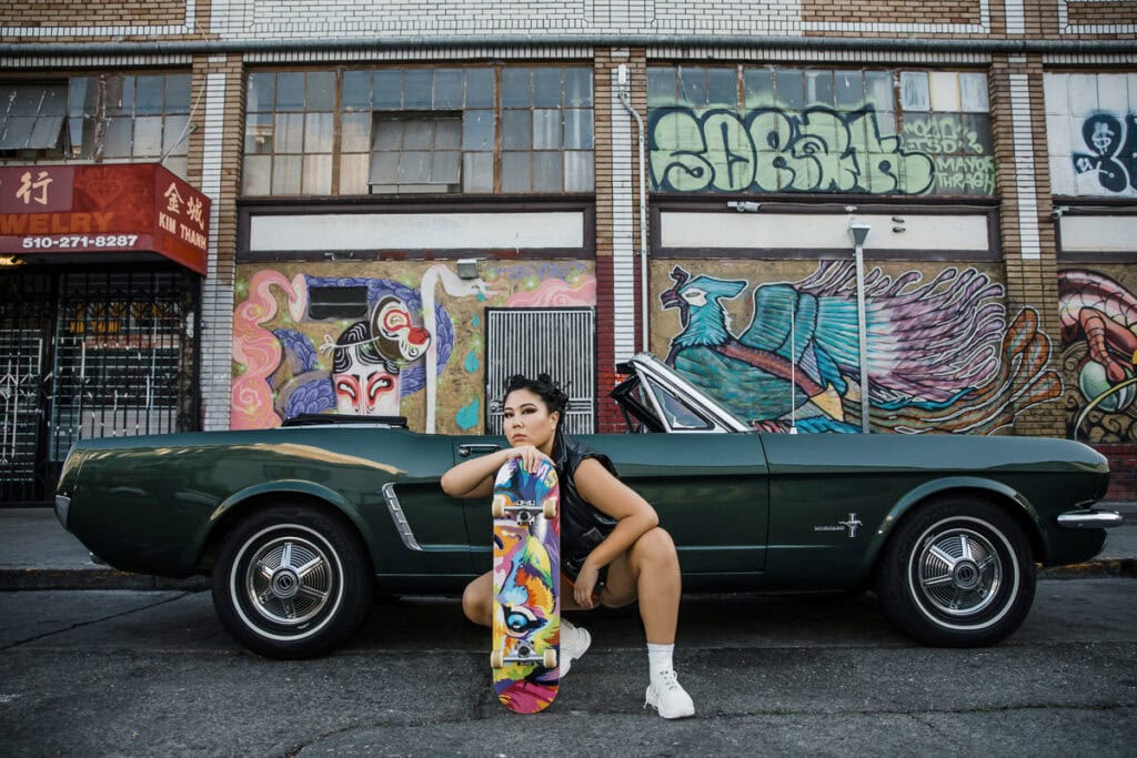Woman with skateboard leaning on vintage green car in front of graffiti wall. -Oakland Branding Photography