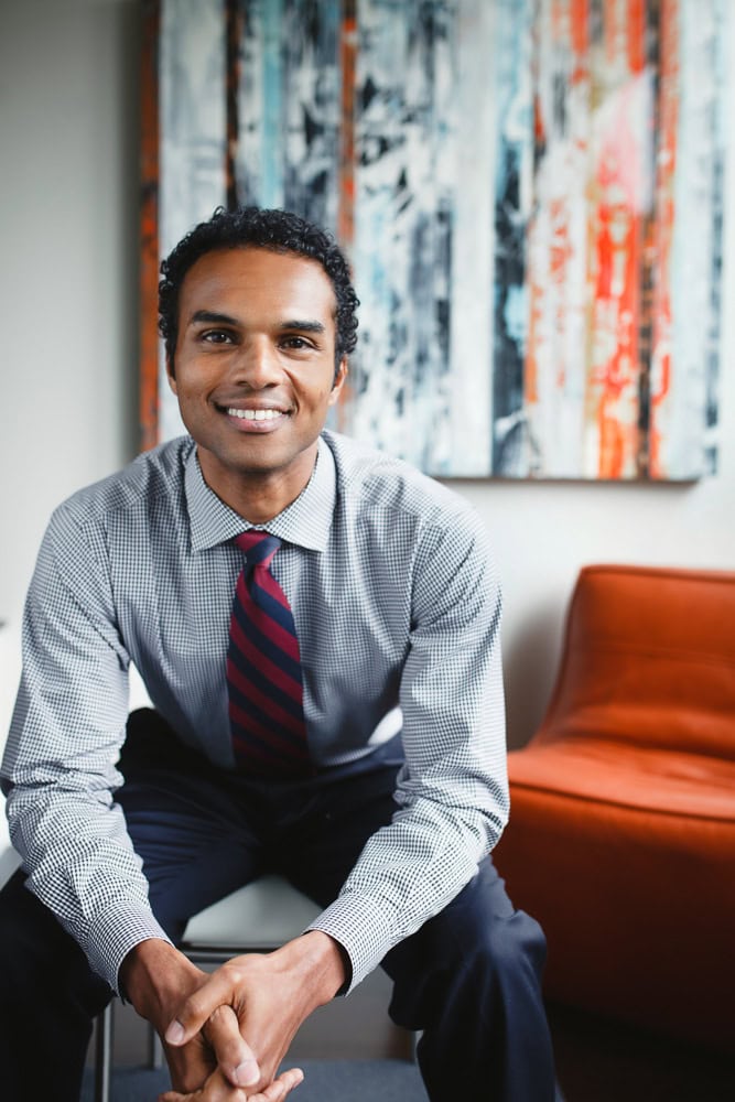 Confident businessman smiling in office setting with colorful abstract art behind him.