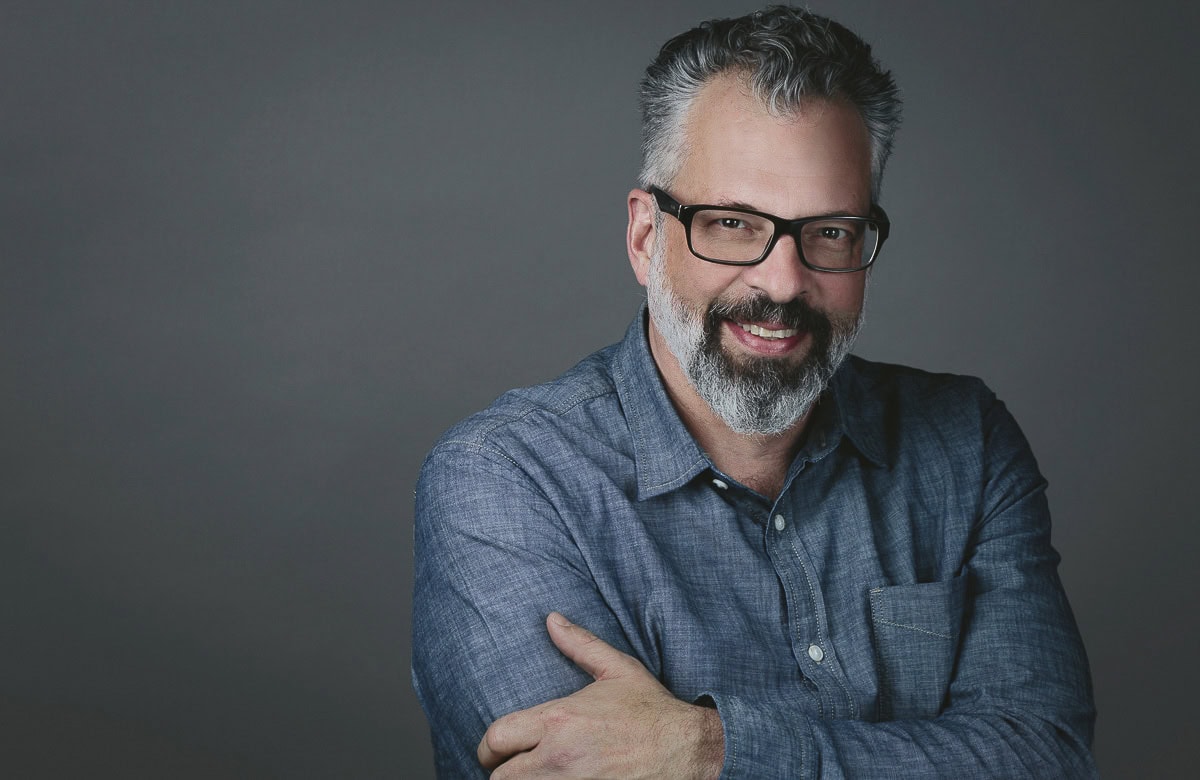 A professional headshot of a smiling man wearing glasses and a blue shirt- Becca Henry Photography