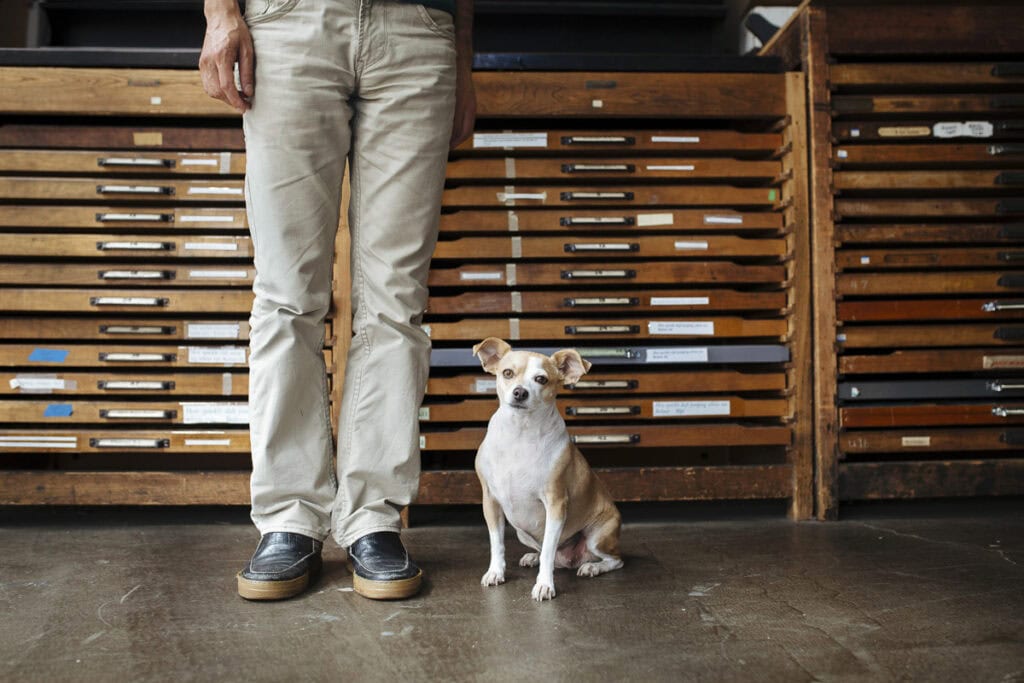 Image of person with cute dog in front of wooden shelves for San Francisco Center for the Book 