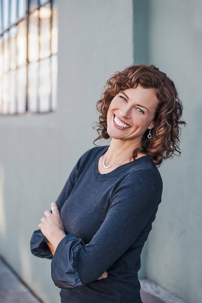 Smiling woman with curly hair in a navy sweater, outdoor branding photo.