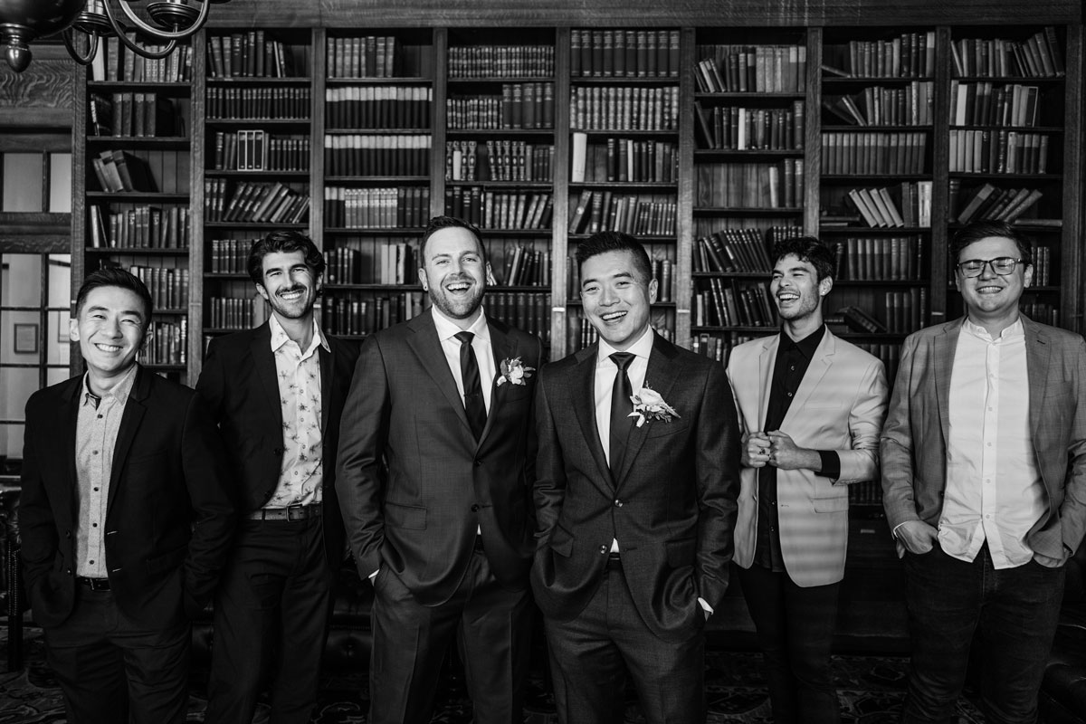 Groomsmen in suits celebrating at a library with bookshelves in the background.
