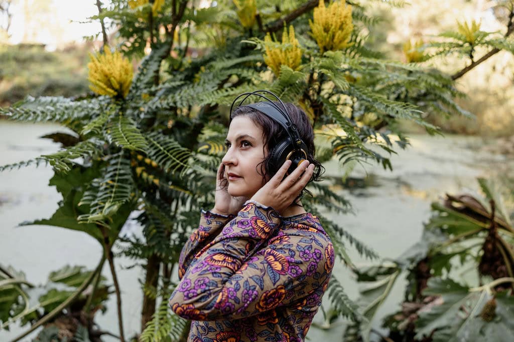 Woman enjoying music with headphones in lush natural setting.