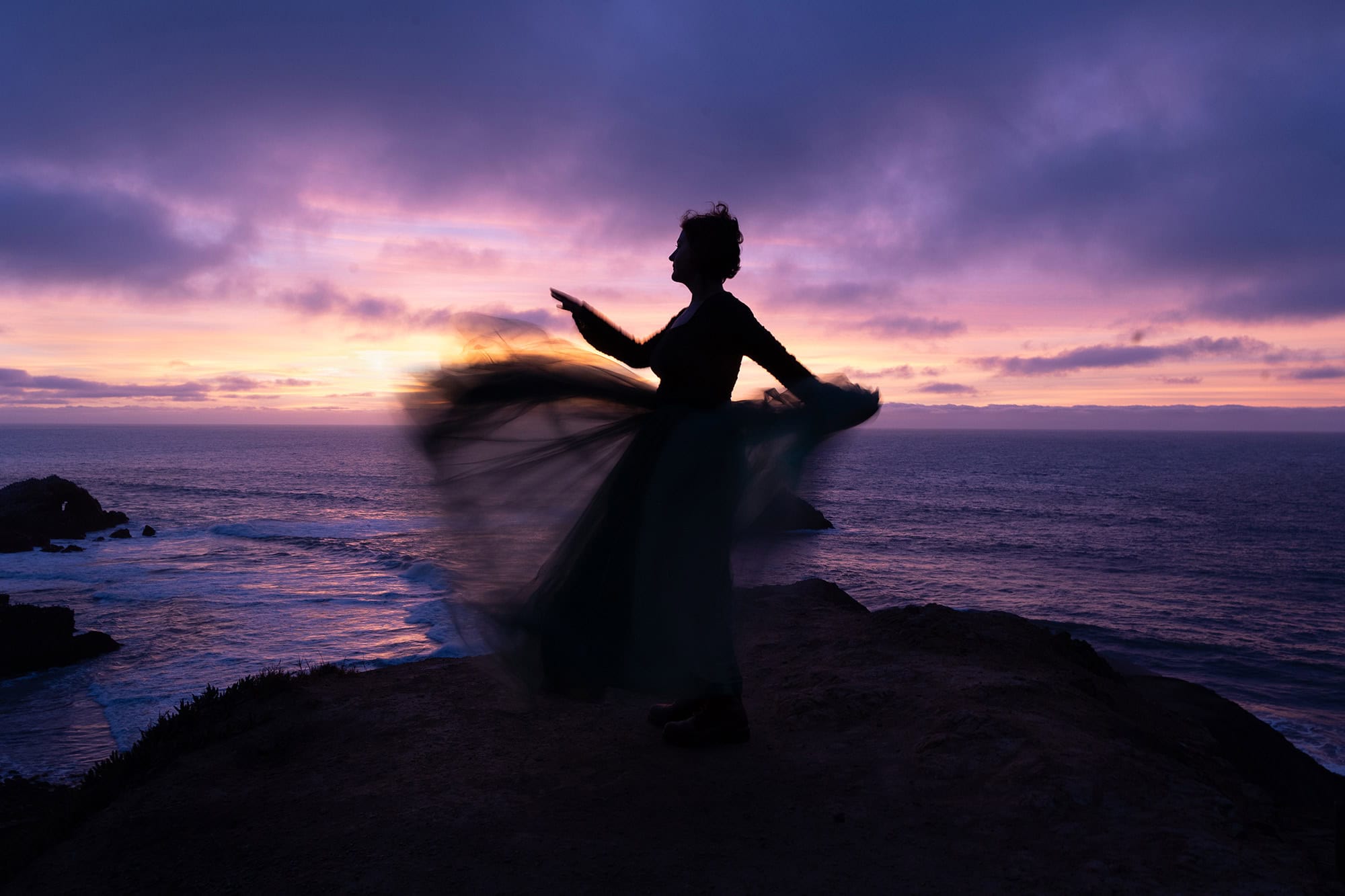 Elegant silhouette of a woman on a rocky coast at sunset, promoting new branding photography.