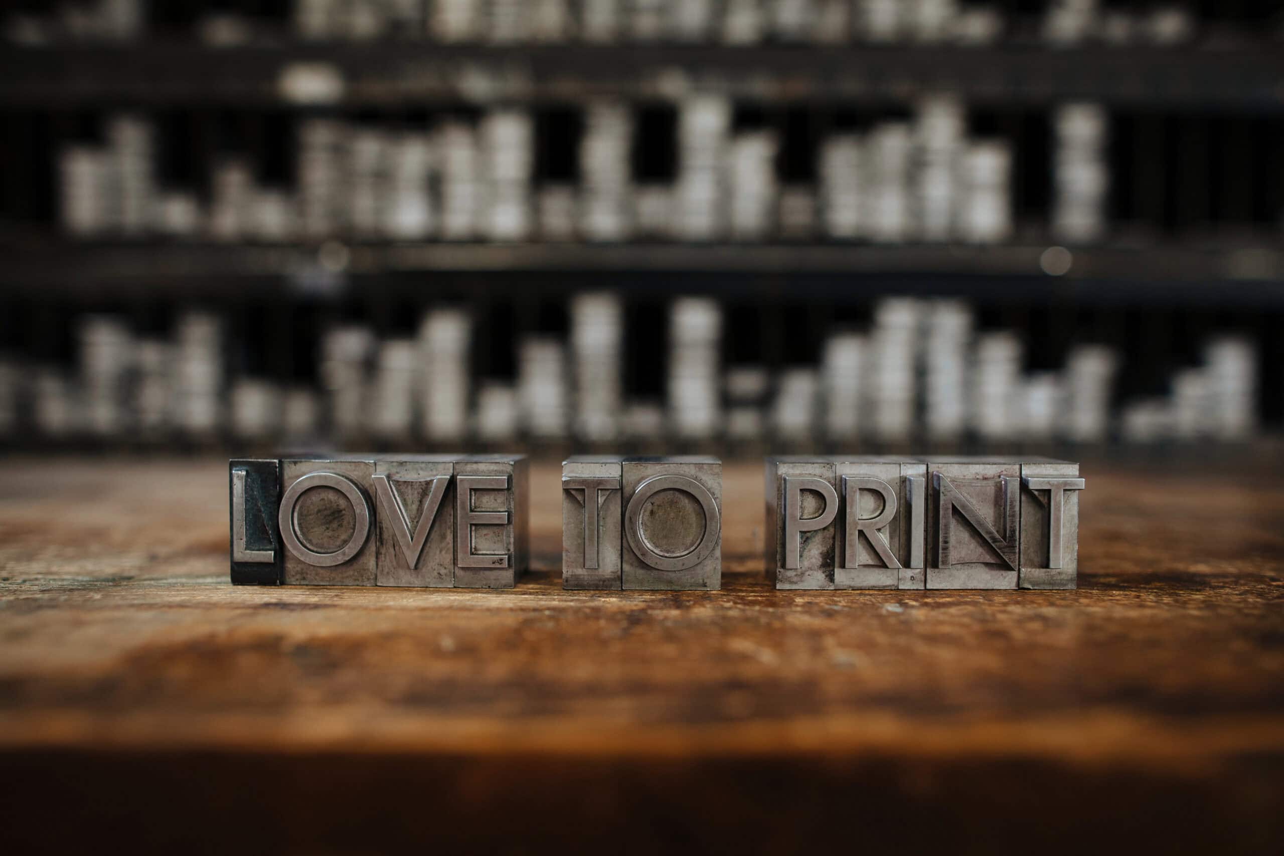 Wooden letter blocks spelling "LOVE TO PRINT" on a rustic surface with blurred background.