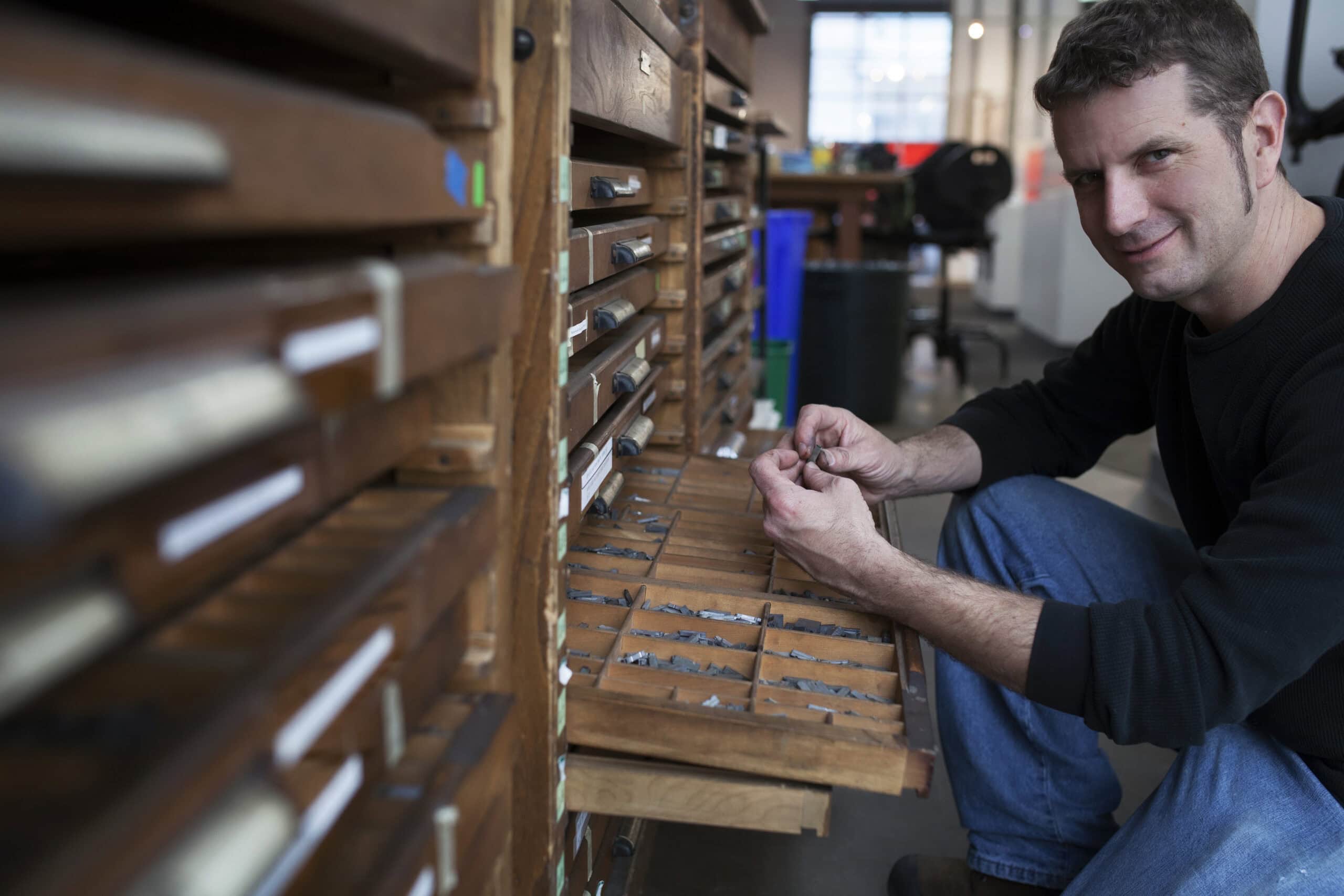 Man working with vintage wooden drawers in a creative workspace.