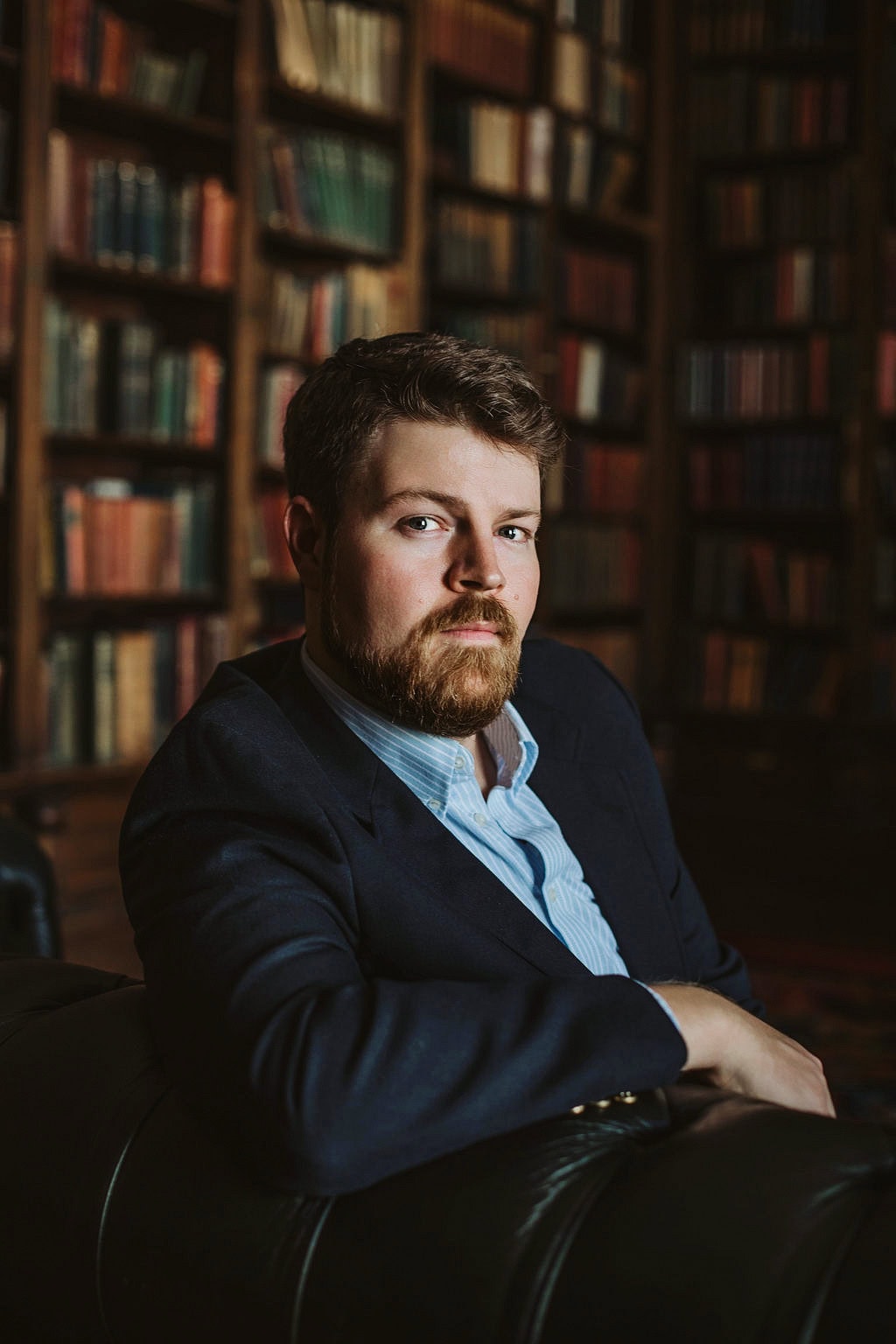 Professional portrait of a man in a library with bookshelves in the background.
