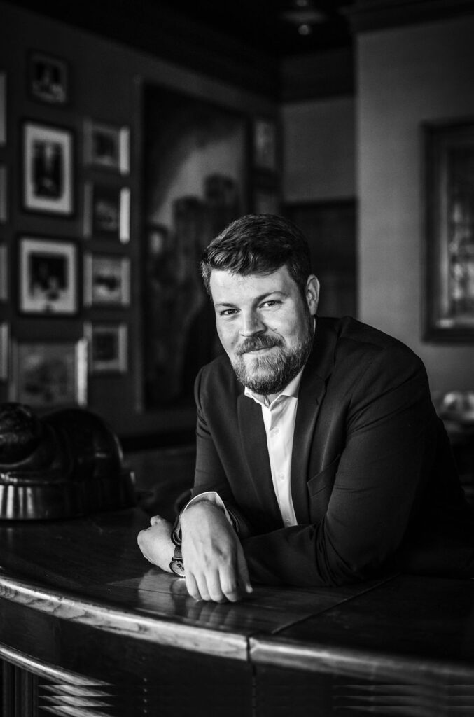 Professional portrait of a man in a suit at a bar, showcasing branding and corporate identity.